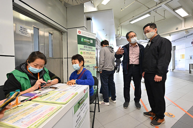 The Secretary for Innovation and Technology, Mr Alfred Sit (first right), visits the Hong Kong Health Code mobile support station located at Tai Po Market MTR Station today (December 25) and is briefed by the Assistant Government Chief Information Officer (Industry Development), Mr Kingsley Wong (second right), on the operation of the outreach team in assisting citizens in need to make applications for the Hong Kong Health Code.